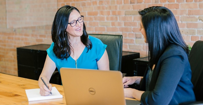 Two business professional women smiling at each other. 