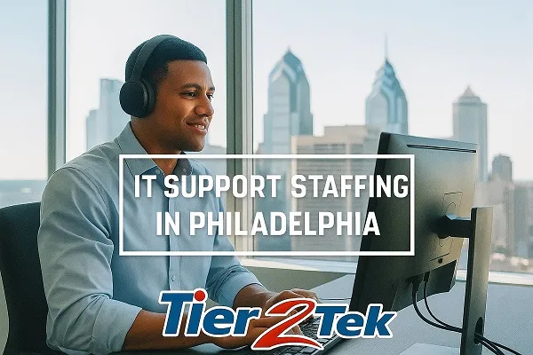 Young IT professional working on desktop support tasks with the Philadelphia skyline in view, representing Tier2Tek Staffing’s IT support staffing services.