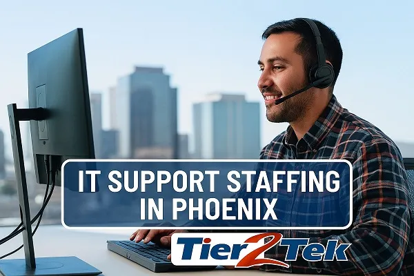 Young IT support professional working at a desk with Phoenix city skyline in the background, representing Tier2Tek Staffing’s IT support staffing services.